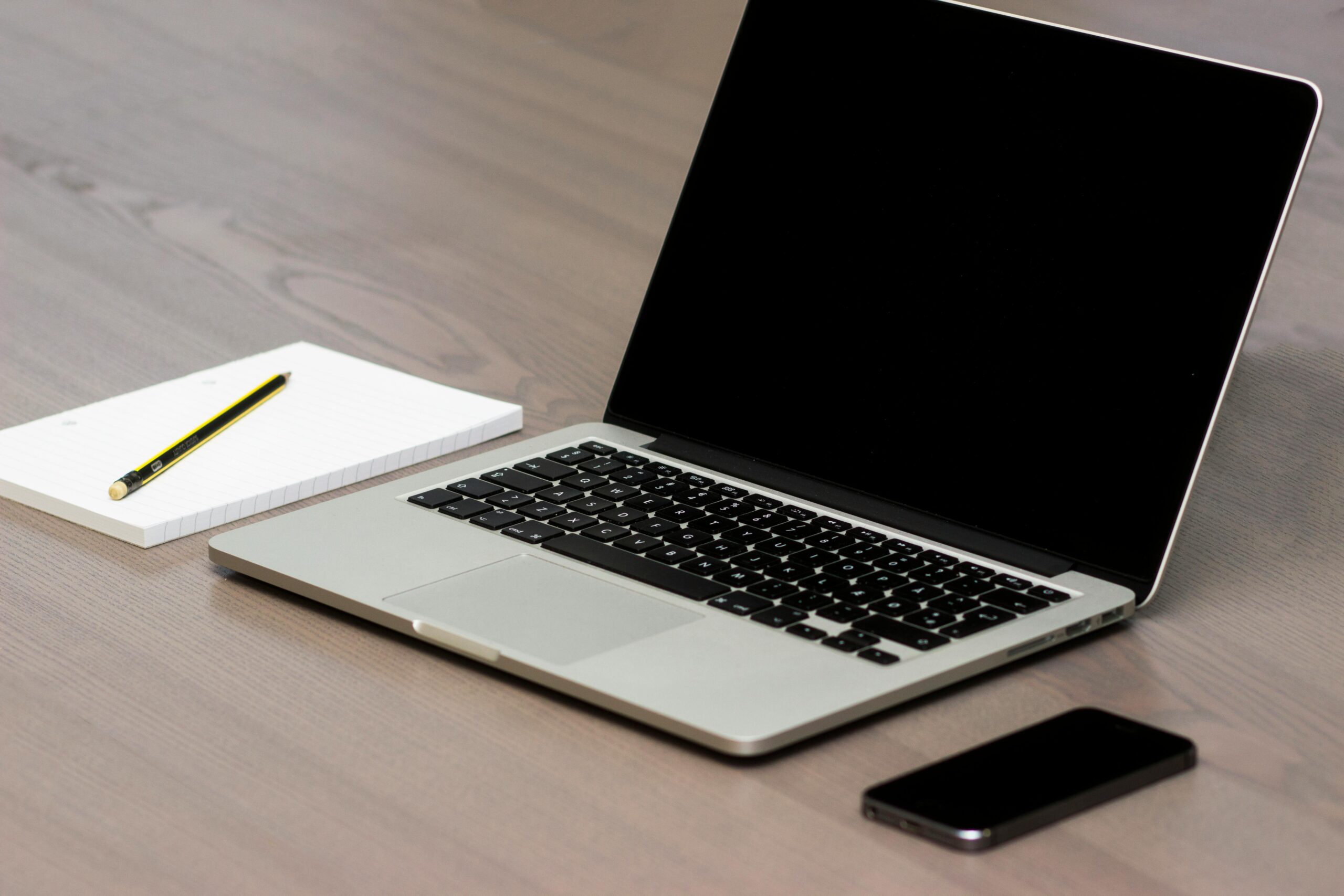 Used laptop with notepad and smartphone on wooden desk, representing considerations for buying second-hand computers