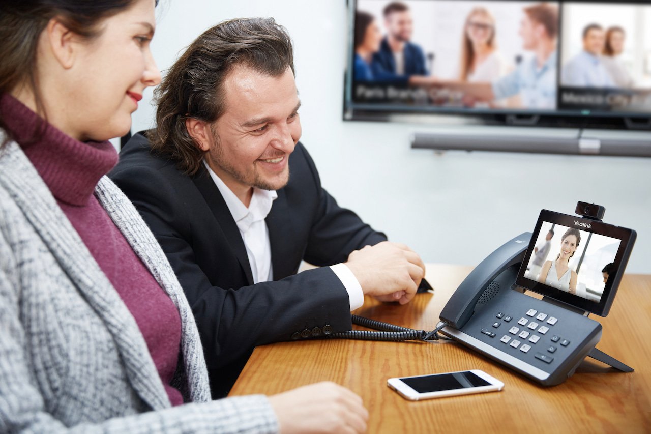 Two business professionals on a video call using a Yealink VoIP desk phone, illustrating Illini Tech Services’ advanced communication solutions