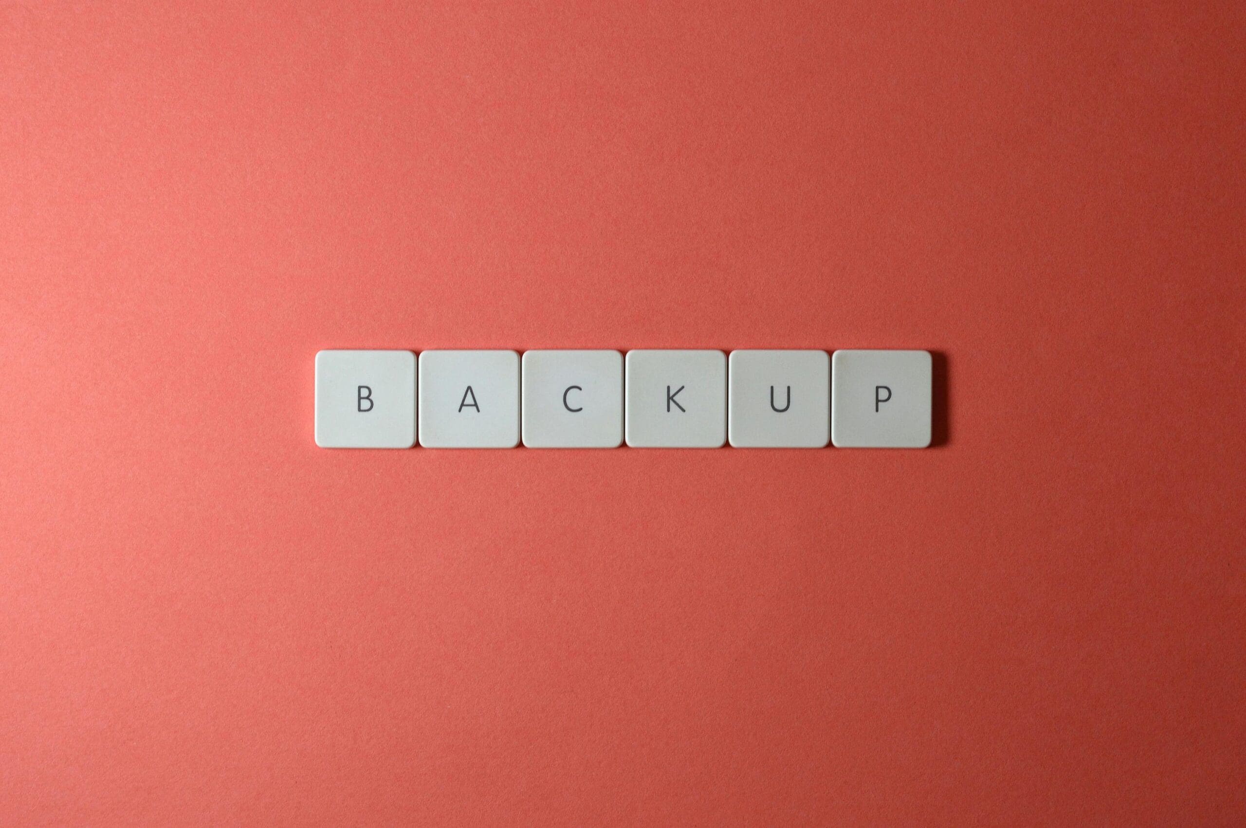 White keyboard keys arranged to spell "BACKUP" on a red background, symbolizing digital data protection and recovery planning.