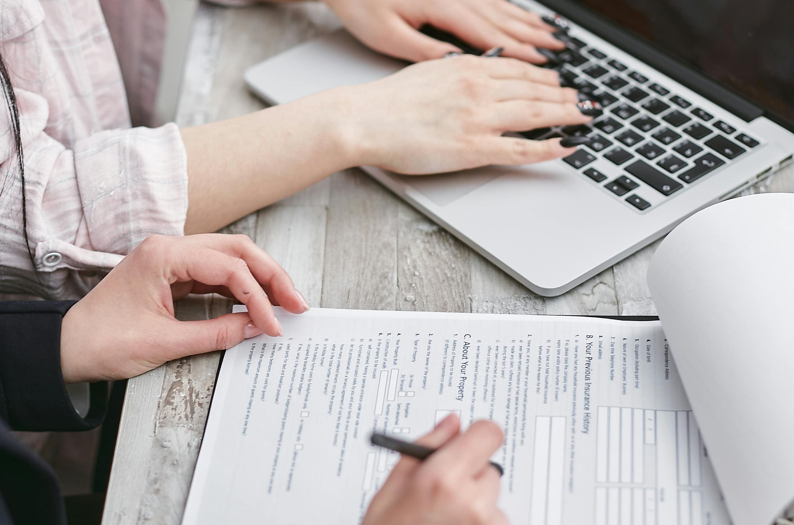 Close-up of hands filling out insurance paperwork beside a laptop, representing the intersection of cybersecurity and business risk management.
