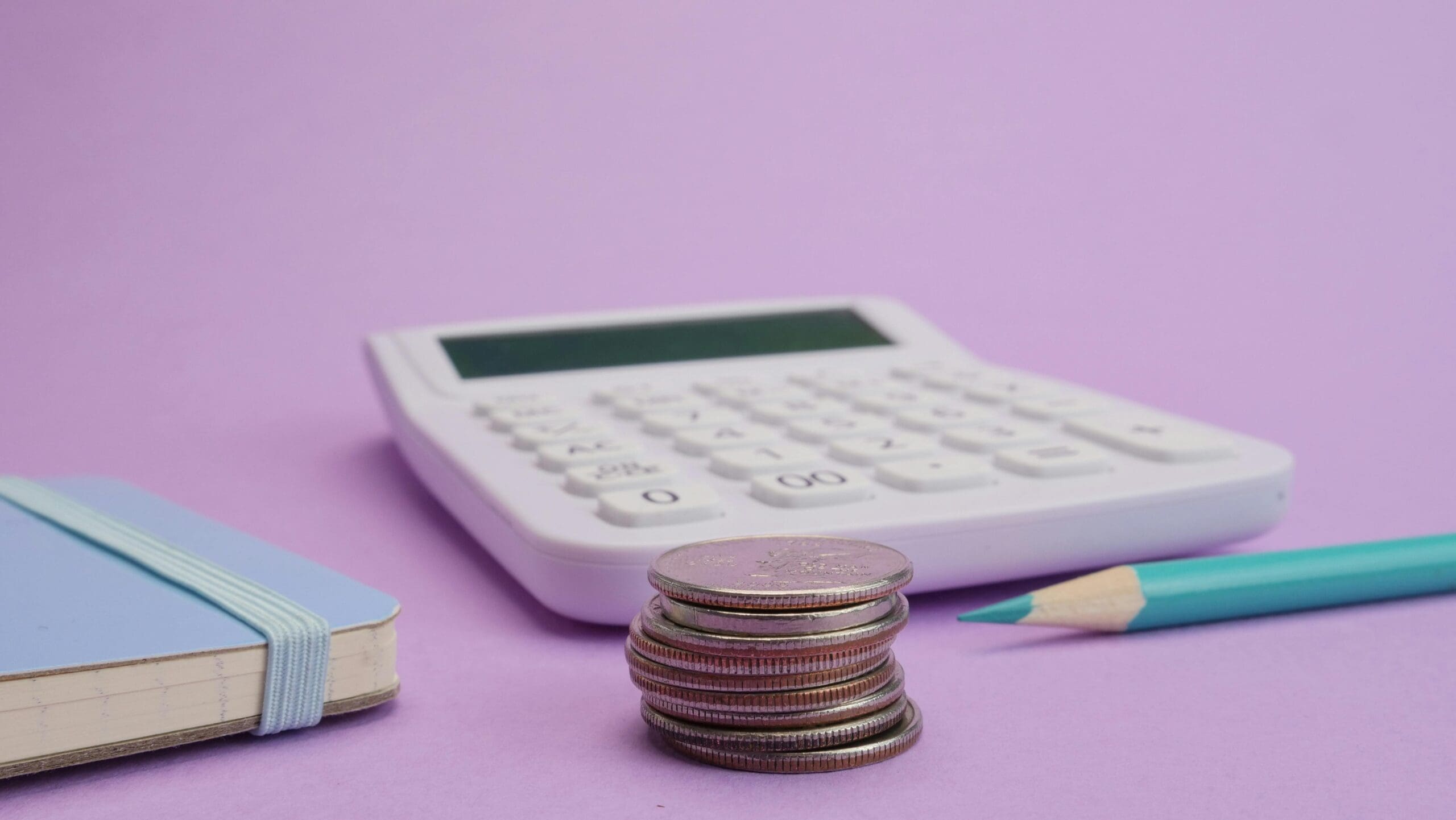 Stack of coins, calculator, and pencil on a pastel background representing cloud cost management and small business budgeting.